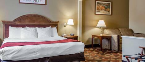 Habitación de hotel con una cama grande, dos lámparas de noche, una silla, una mesita y un cuadro en la pared.