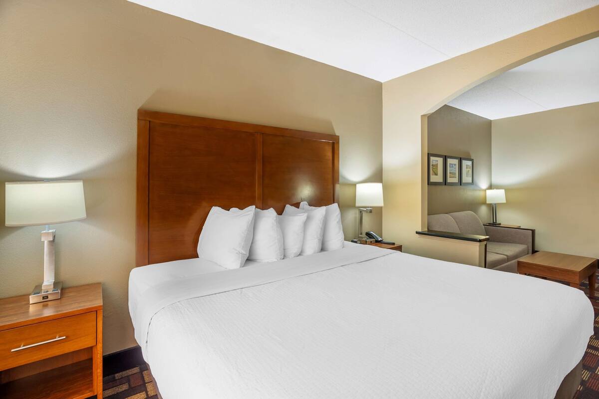 A hotel room with a large bed, two bedside tables, a nightstand, a chair, a desk, and a mirror.