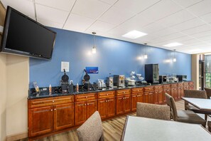 A hotel breakfast area with a long counter, wooden cabinets, a flat-screen TV, and seating. - Best Western Grantville/hershey (Grantville)