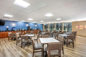 A spacious dining area with tables and chairs, a kitchen area with appliances, and large windows providing natural light. - Best Western Grantville/hershey (Grantville)
