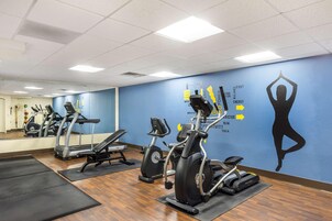 Un gimnasio con cintas de correr, bicicletas estáticas y una pared con gráficos de ejercicios.