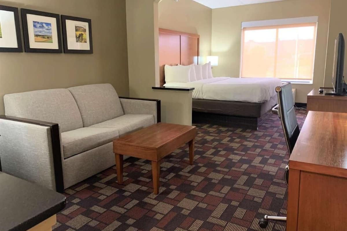 A hotel room with a sofa, a bed, a wooden coffee table, a TV, and framed pictures on the wall.