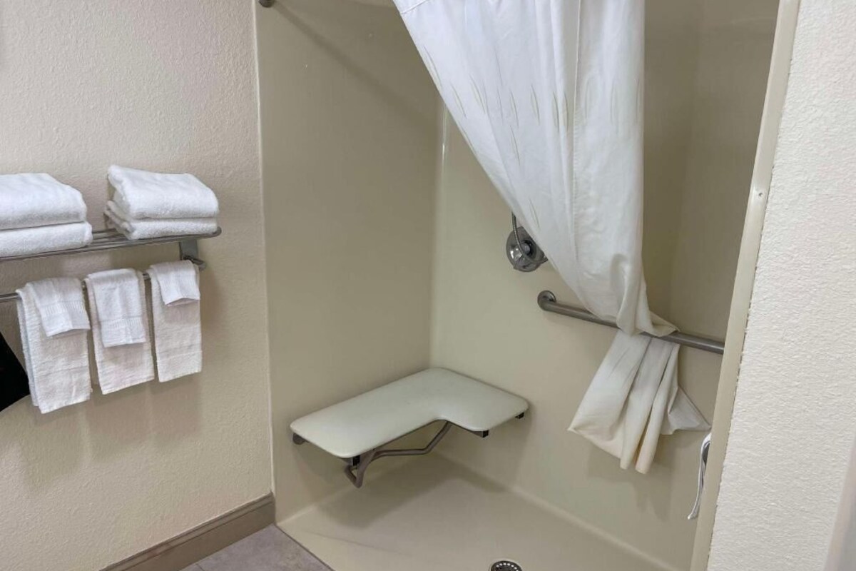 A shower area with a white shower curtain, a bench, and towels on a rack.