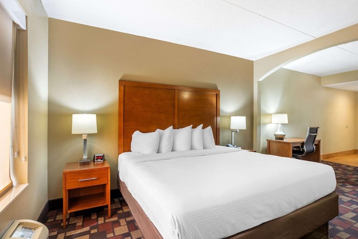 A hotel room with a large bed, two bedside tables with lamps, a desk with a chair, and a mirror on the wall.