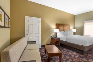 A hotel room with a bed, a sofa, a nightstand with a lamp, and a patterned carpet.