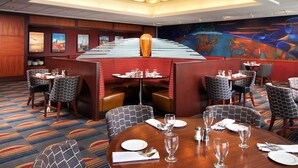 A hotel dining area with multiple tables and booths, a large mural on the wall, and a patterned carpet. - Cleveland Airport Hotel (Cleveland)