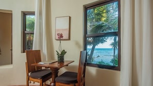 Una habitación con una mesa y sillas de madera, una planta en maceta, un cuadro enmarcado y vista al océano a través de un ventanal grande.