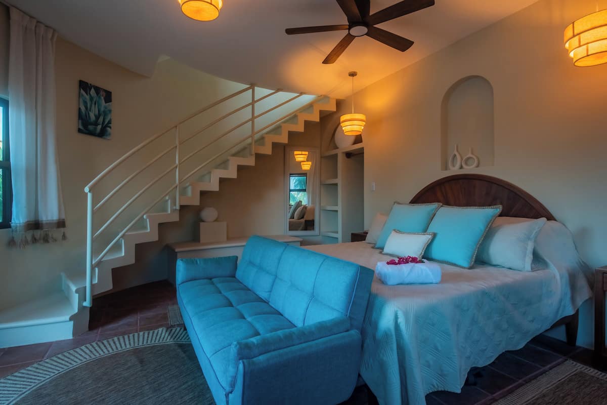 A bedroom with a bed, a blue sofa, a staircase, and a ceiling fan.