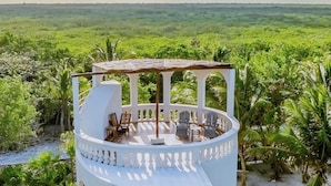 Un edificio blanco de varios niveles con mesas al aire libre y vistas a un paisaje exuberante.