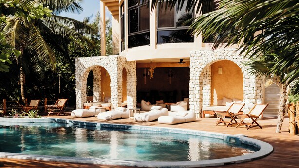 Un área de piscina con arcos de piedra, sillones de descanso y una terraza de madera.