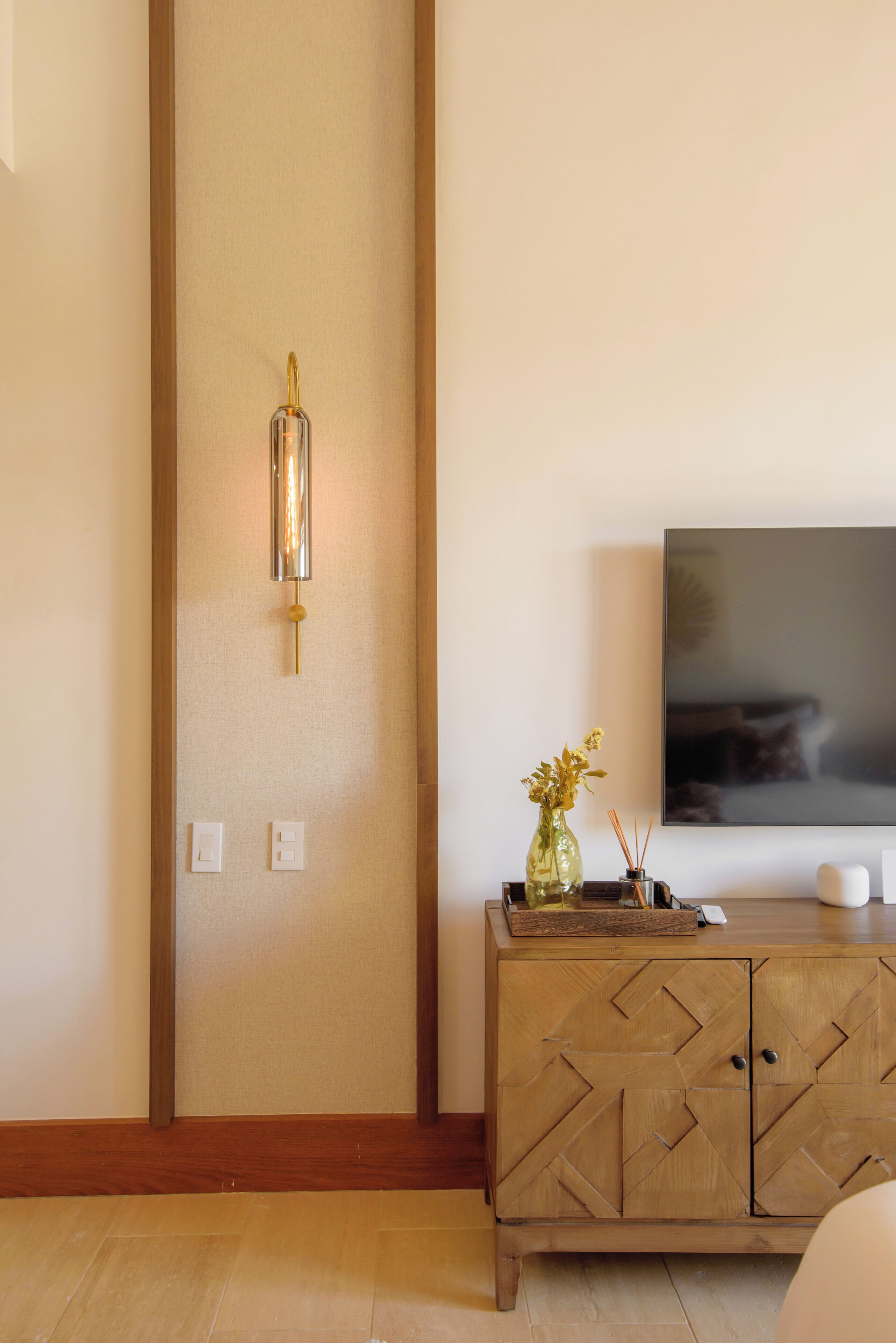 Un salon moderne avec un meuble en bois, un luminaire fixé au mur et un téléviseur à écran plat.
