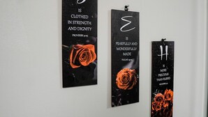 Drei vertikale Schilder mit Text und Rosenmotiv, an einer Wand befestigt.