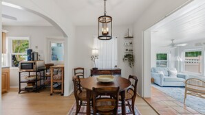 Un coin repas avec une table ronde en bois, six chaises, un lustre et une vue sur l’extérieur.