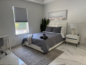 A bedroom with a bed, bedside table, lamp, and a window with blinds. - Stylish 4BR /2 Bath Oasis with Heated Pool, Hot Tub - 10 Mins to Beach/Downtown (West Palm Beach)