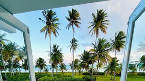 A balcony with glass doors, a view of palm trees, and a grassy area. - Villa Del Mar – Beachfront Luxury Home with Private Pool & Ocean Views (Punta Santiago)