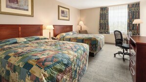 A hotel room with two beds, a desk, a chair, and a window with curtains.