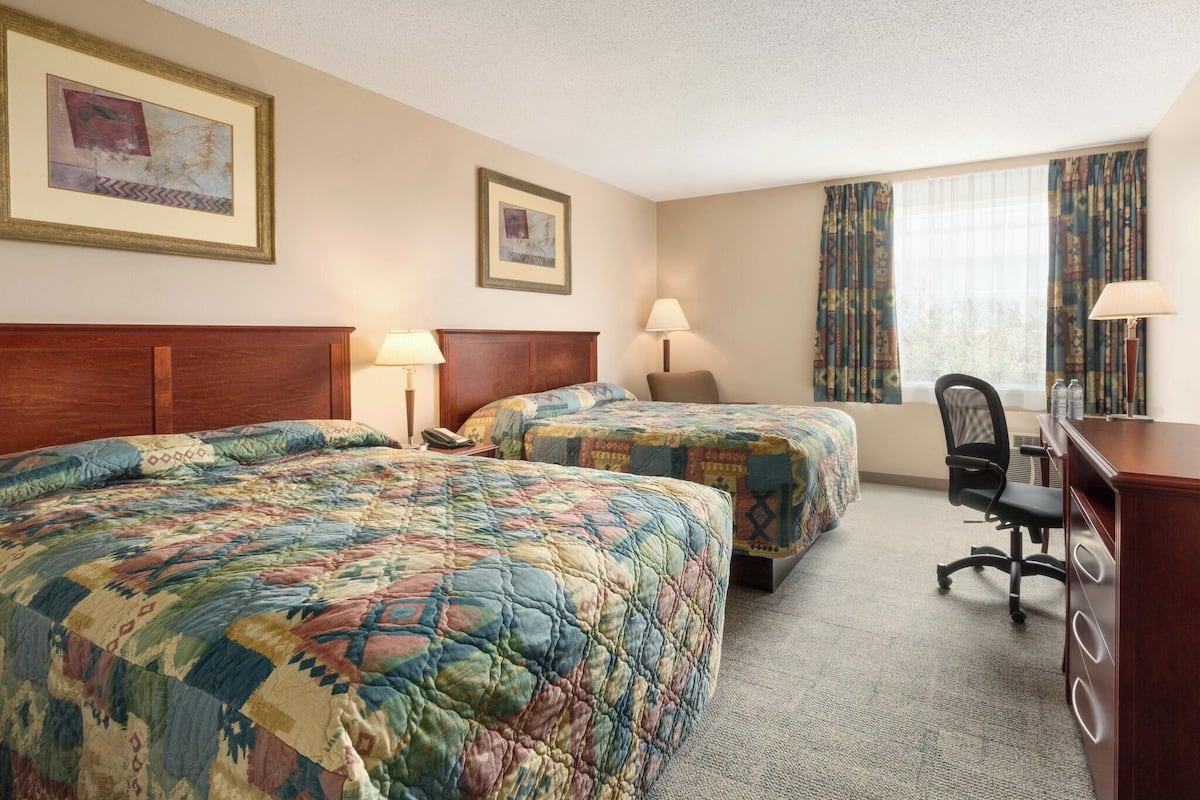 A hotel room with two beds, a desk, a chair, and a window with curtains.