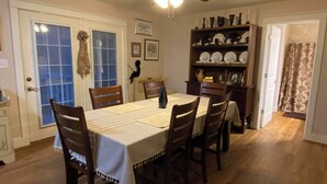 Zona pranzo con tavolo apparecchiato per sei persone, sedie in legno, ventilatore a soffitto e mensola con stoviglie.