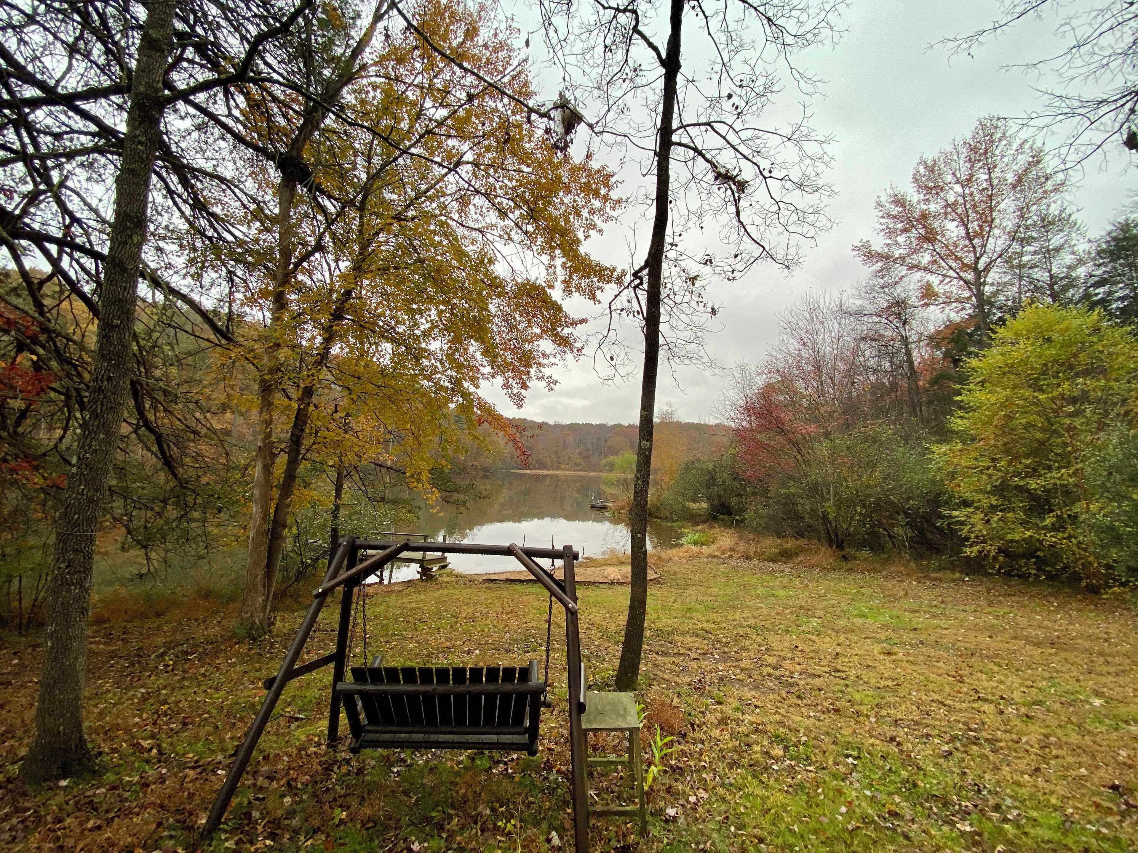 A wooden swing set in a wooded area with a lake in the background.