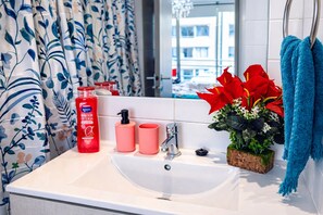 A bathroom with a white sink, red and pink toiletries, a potted plant, and blue towels. - Metro cal y canto two bedrooms free wifi (Santiago)