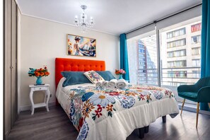 A modern bedroom with a large bed, a painting, a chandelier, and a view of a building. - Metro cal y canto two bedrooms free wifi (Santiago)
