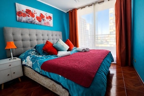 A modern bedroom with a grey tufted headboard, a blue and red patterned bedspread, and a red throw blanket. - Metro Plaza de Armas, 2-room apartment, Wi-Fi, 24/7 check-in (Santiago)