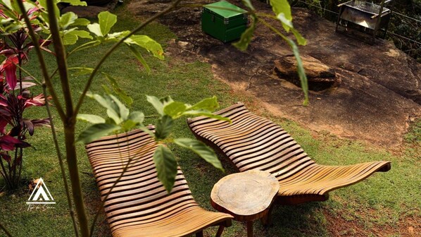 Deux fauteuils de jardin en bois, dotés d’un design incurvé original, sont placés sur une pelouse, avec une table en bois entre les deux.