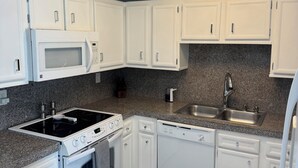 Cozinha moderna com armários brancos, micro-ondas embutido, fogão, forno e lava-louças, além de bancada de granito.