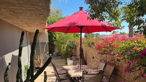 Um pátio com mesa e cadeiras, um guarda-sol vermelho e uma planta cacto.