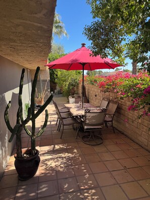 A patio with a table and chairs, a red umbrella, and a cactus plant. - Palm Springs Tranquility (Palm Springs)