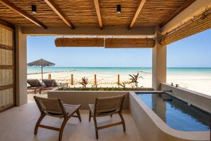 Un balcón con vista a la playa, dos sillones de mimbre, una piscina y un techo de paja.