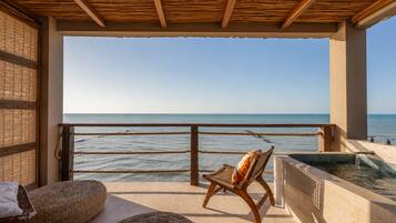 Balcón con vista al mar, una silla, un jacuzzi pequeño y esteras tejidas.