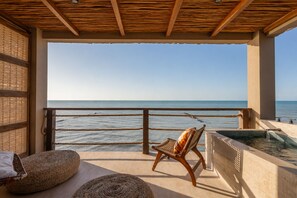 Balcón con vista al mar, una silla, un jacuzzi pequeño y esteras tejidas.