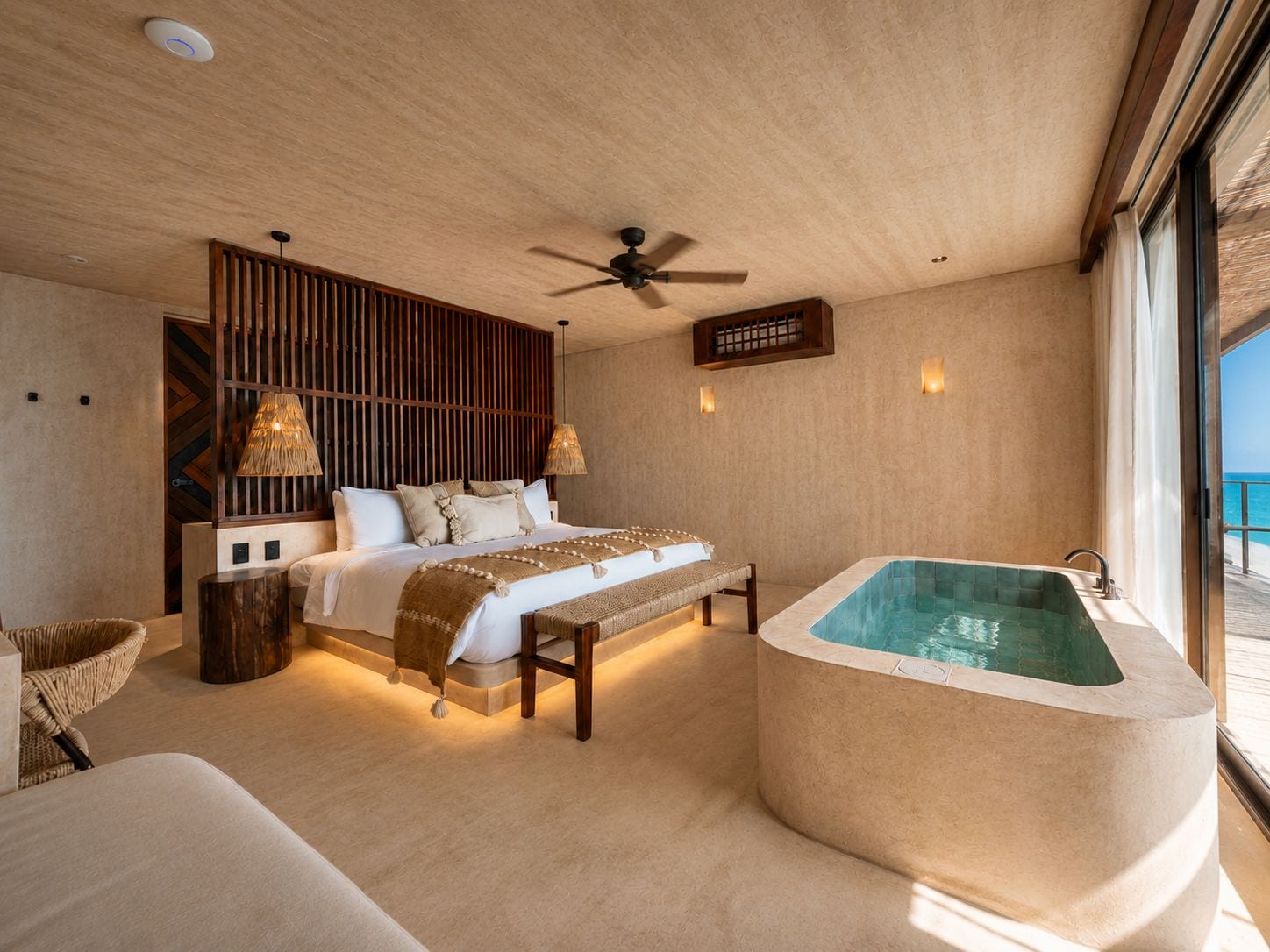 Ein Schlafzimmer mit einem großen Bett, einem hölzernen Kopfstück, einer Sitzbank, einer Badewanne und Meerblick.