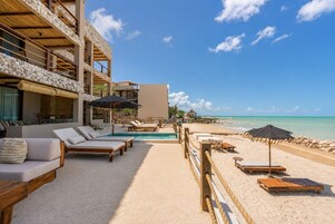 A beachfront hotel with a pool, sun loungers, and a view of the ocean.
