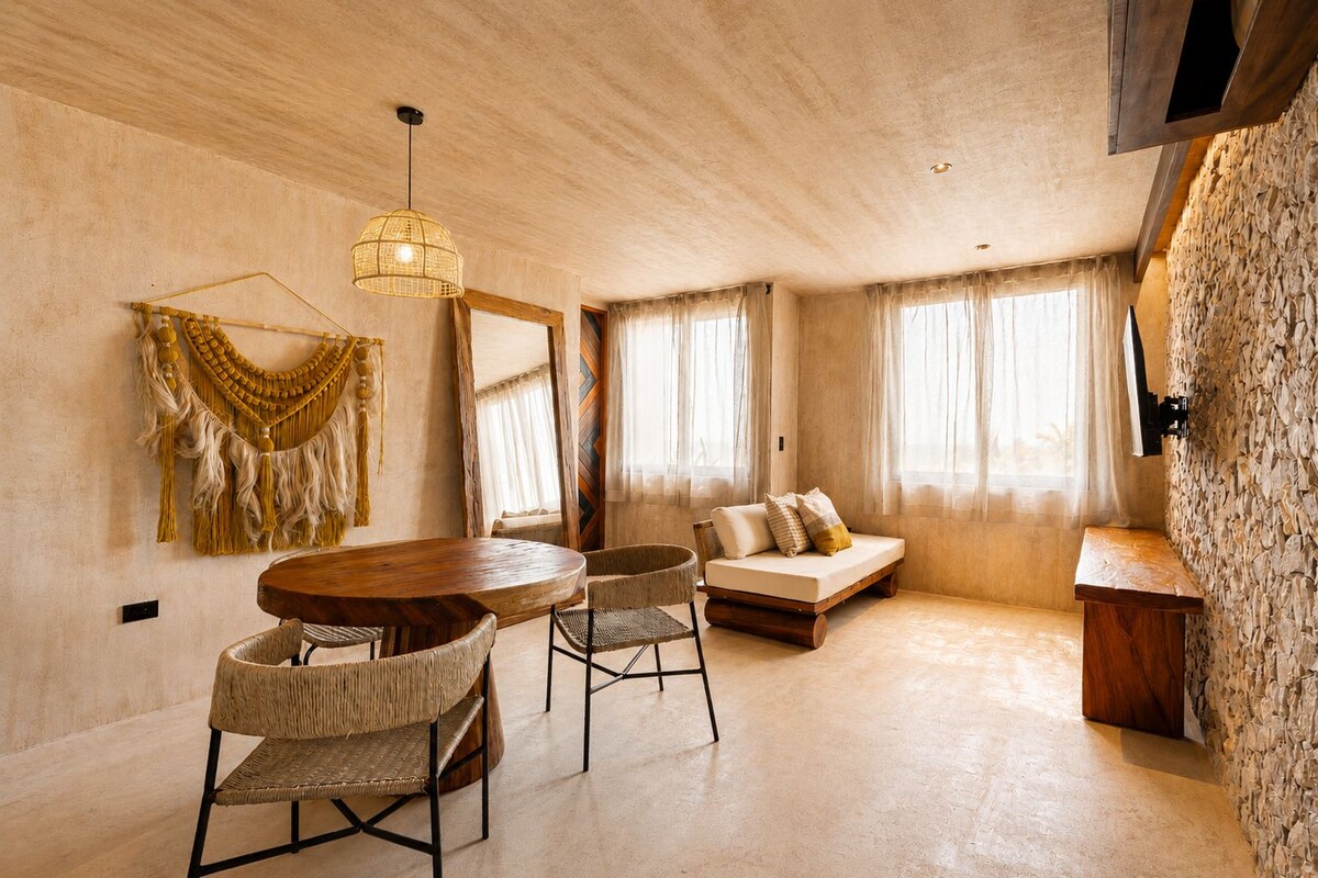 A cozy living area with a wooden dining table, woven chairs, a sofa, and a hanging light fixture.