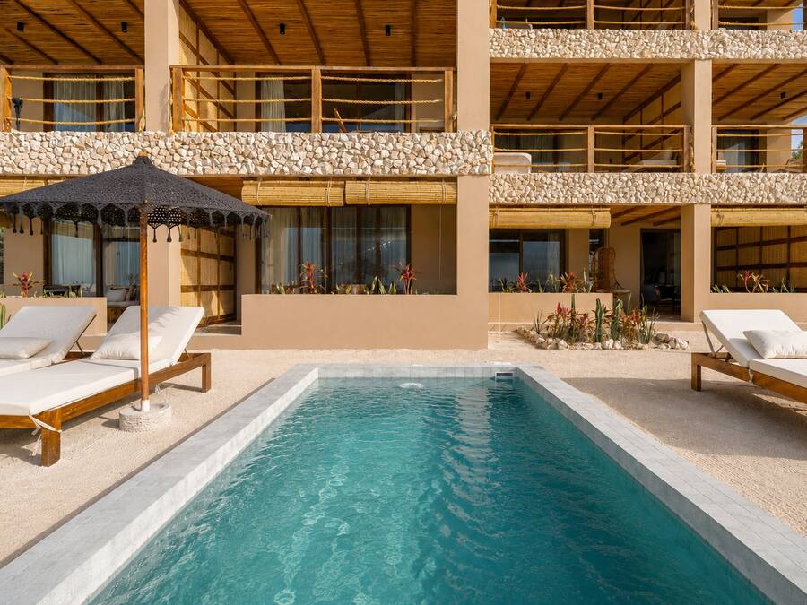 Un área junto a la piscina con sillones de descanso y una sombrilla.