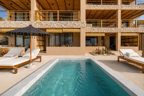 Un área junto a la piscina con sillones de descanso y una sombrilla.