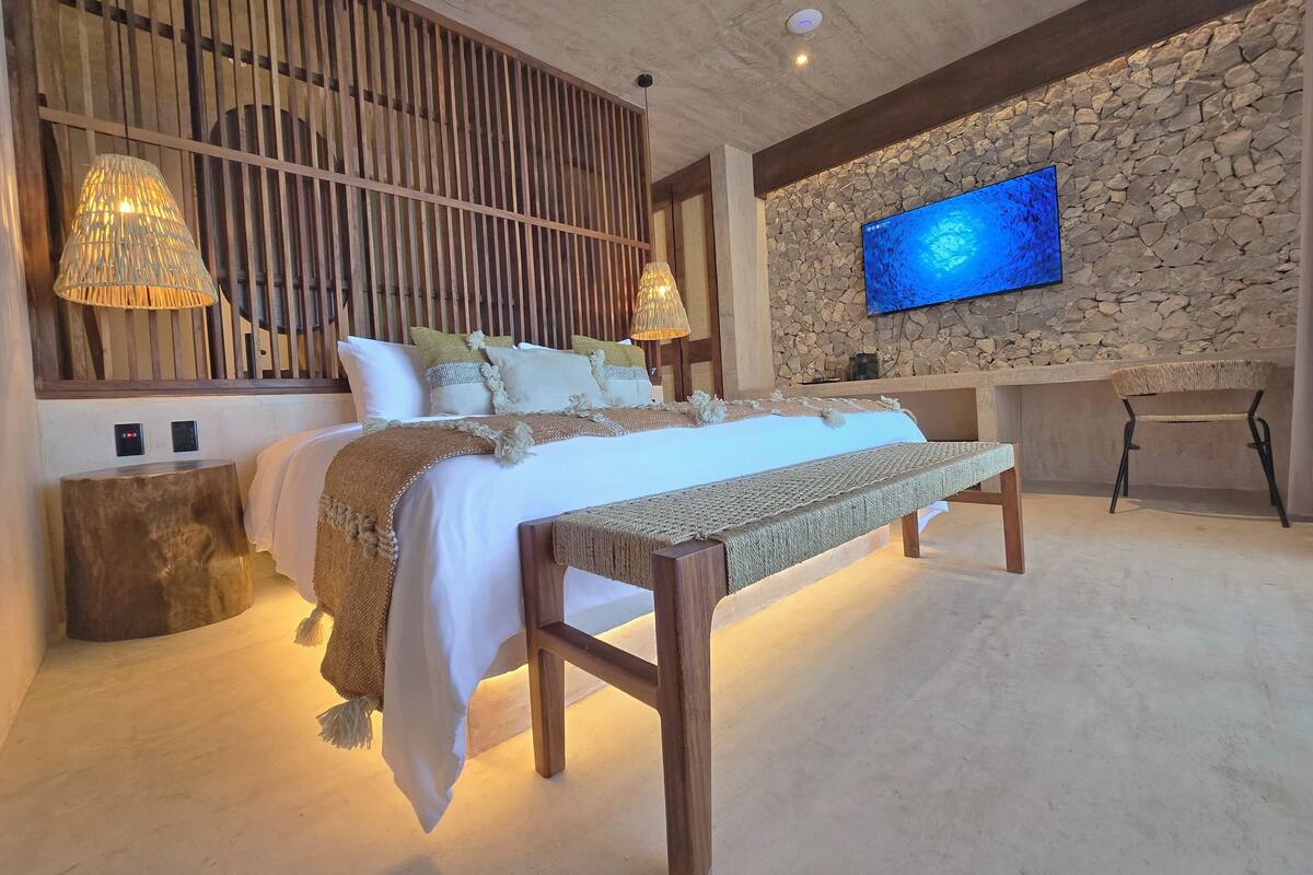 A modern bedroom with a bed, bedside lamps, a stone wall, a television, and a desk.