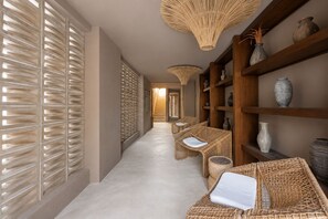 Un pasillo con muebles de mimbre, estantes con jarrones y una pared con textura.