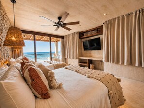 Un dormitorio con una cama grande, ventilador de techo, televisión y vista al océano.