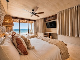 Une chambre avec un grand lit, un ventilateur de plafond, une télévision et une vue sur l’océan.
