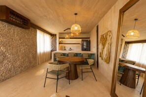 A modern kitchen with a stone wall, a dining area with a round table and wicker chairs, and a hanging light fixture. - Luxury Villas By Awa Holbox - Beachfront (Isla Holbox)