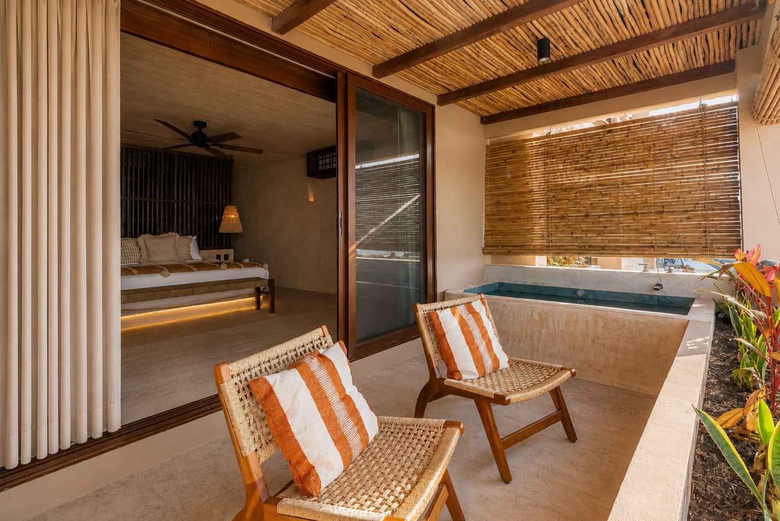 Una habitación con cama, ventana con persianas, ventilador de techo y un pequeño área de piscina con sillas.