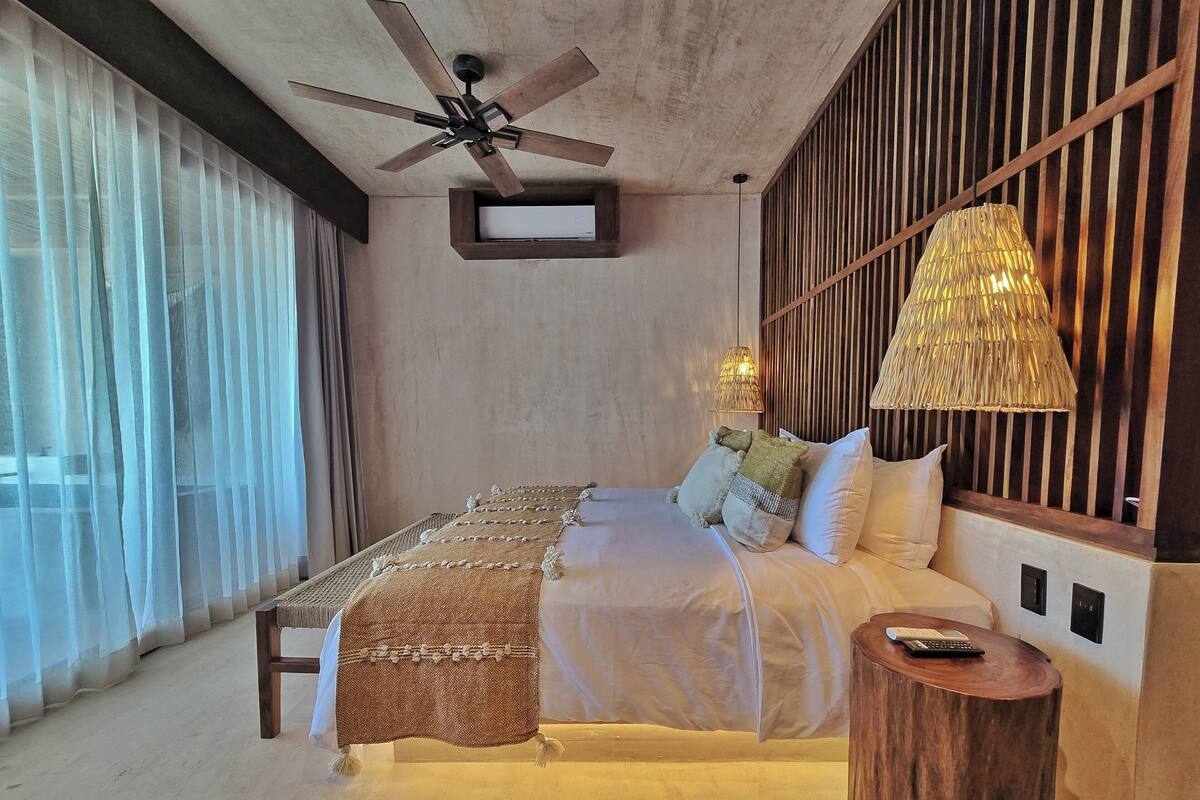 A modern bedroom with a bed, a ceiling fan, a bedside lamp, and a wooden nightstand.
