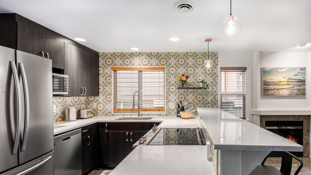 A modern kitchen with dark wood cabinets, stainless steel appliances, a large island, and patterned backsplash. - Spacious Roosevelt Urban Lodge + Walk to Light Rail (Seattle)