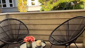 A balcony with two black wire chairs, a small round table with a vase of flowers and a mug, and a patterned rug. - Spacious Roosevelt Urban Lodge + Walk to Light Rail (Seattle)