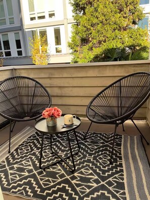 A balcony with two black wire chairs, a small round table with a vase of flowers and a mug, and a patterned rug. - Spacious Roosevelt Urban Lodge + Walk to Light Rail (Seattle)