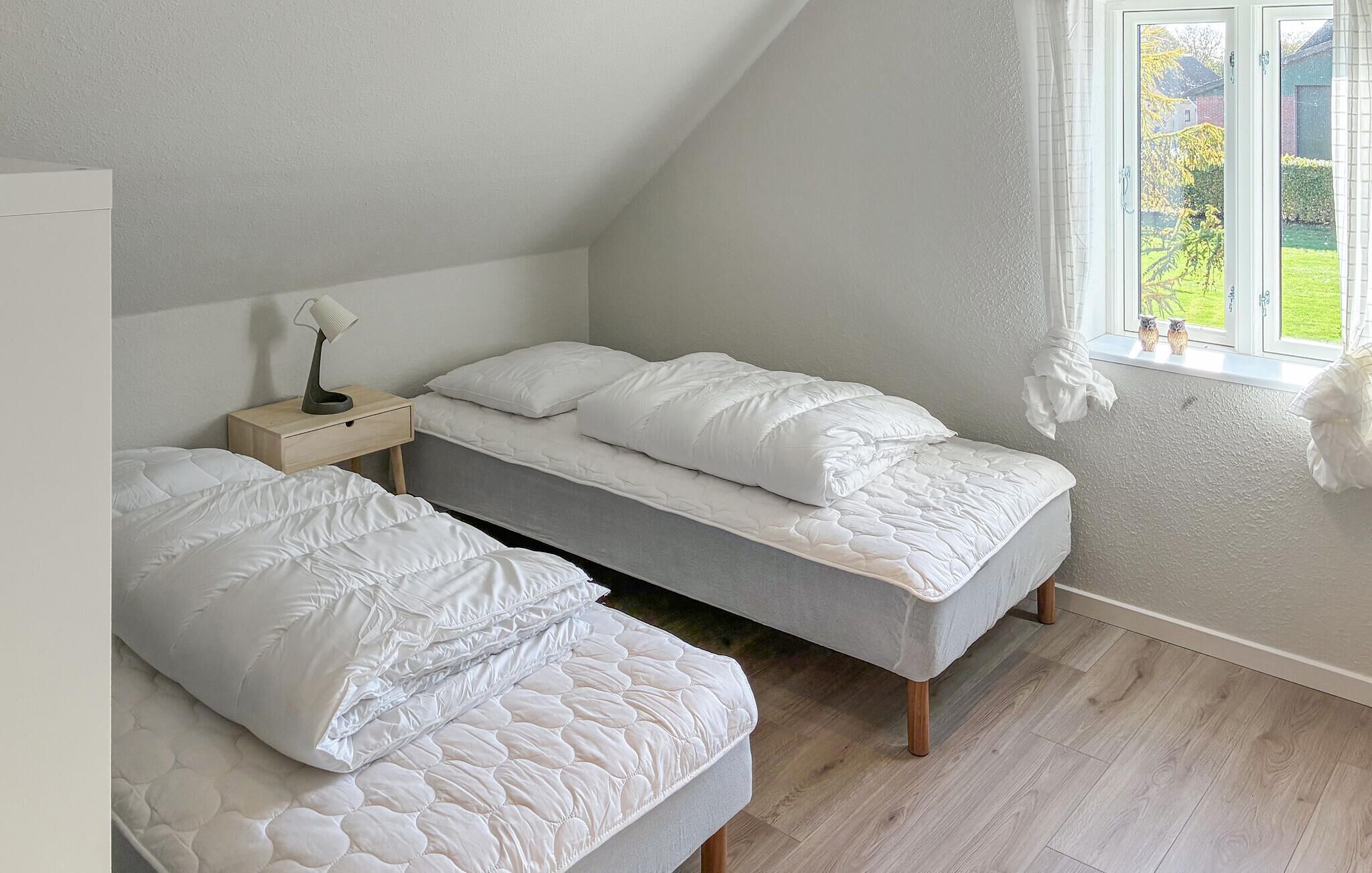 Une chambre avec deux lits simples, une table de chevet avec une lampe et une fenêtre donnant sur l’extérieur.