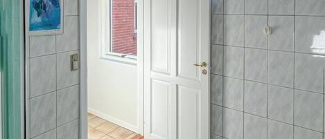 A hallway with a white door, a window with a view of a brick wall, and a tiled floor.